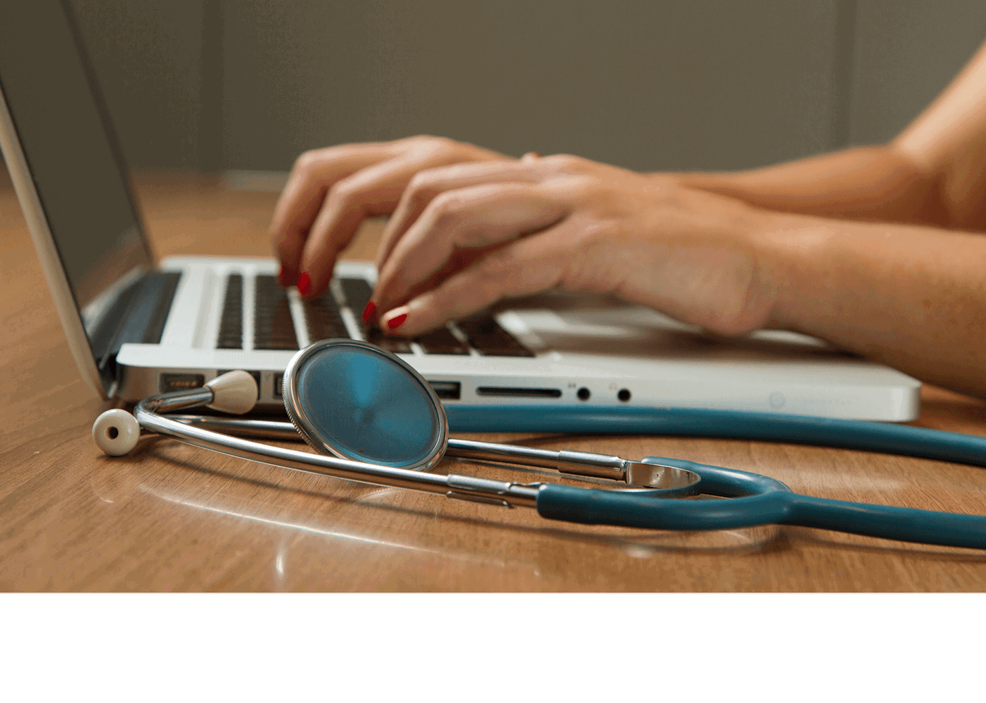 The image shows hands typing on a laptop with a stethoscope nearby, suggesting a healthcare professional at work.
